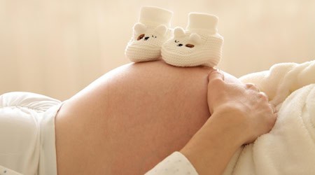 Babyschuhe auf Bauch von schwangerer Frau