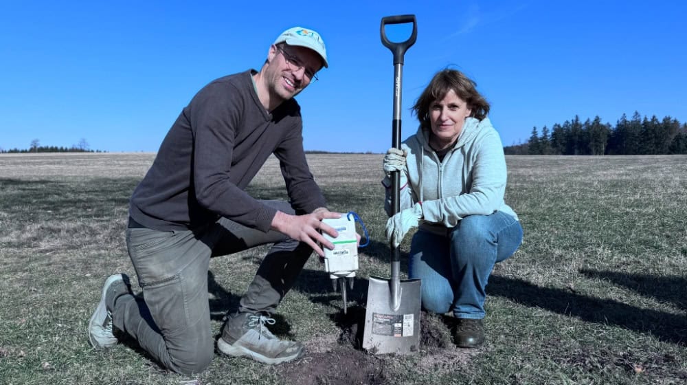 Mit Spaten und Messgerät: Sébastien Delannoy vom Geothermie-erfahrenen Unternehmen TLS Geothermics und Gitta Wahl vom Unternehmen Bestec aus Rheinland-Pfalz zeigen, wie die speziellen Instrumente in die Erde eingebracht werden. Diese Untersuchung des Untergrunds hat den großen Vorteil, dass sie weder spürbar noch hörbar ist und dass sie keinerlei Einschränkungen oder Folgen für die Bevölkerung und Umwelt mit sich bringt. (Bild: Ostvogtland Wärme)