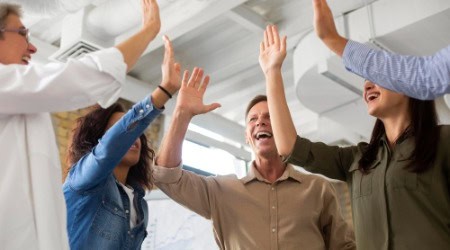 Gruppe fröhlicher Menschen im Büro beim gemeinsamen High-Five – symbolisiert Erfolg, Teamwork und Vertrauen im digitalen Marketing.