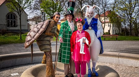 Vier Darsteller:innen in farbenfrohen Kostümen aus „Alice im Wunderland“, darunter Alice, der verrückte Hutmacher, das weiße Kaninchen und die Scheinschildkröte, stehen vor dem Theater in Bautzen.