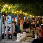 Menschen sitzen unter beleuchteten Bäumen und genießen die offene Atmosphäre der Katzenwirtschaft beim Festival Karierte Katze im Palaisgarten Dresden.
