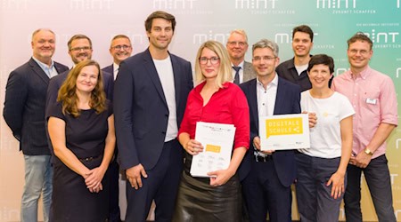 Elf Personen stehen mit Urkunde und Signet "Digitale Schule" vor einer MINT-Fotowand. In der Mitte Digitalbeauftragter Timo Wulff und Schulleiterin Maxi Heß von der Universitätsschule Dresden..