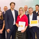 Elf Personen stehen mit Urkunde und Signet "Digitale Schule" vor einer MINT-Fotowand. In der Mitte Digitalbeauftragter Timo Wulff und Schulleiterin Maxi Heß von der Universitätsschule Dresden..