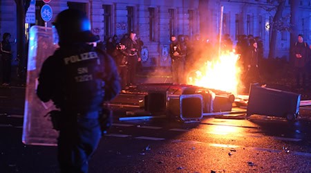 Polizisten stehen auf der Eisenbahnstraße in Leipzig vor brennenden Gegenständen. / Foto: Sebastian Willnow/dpa