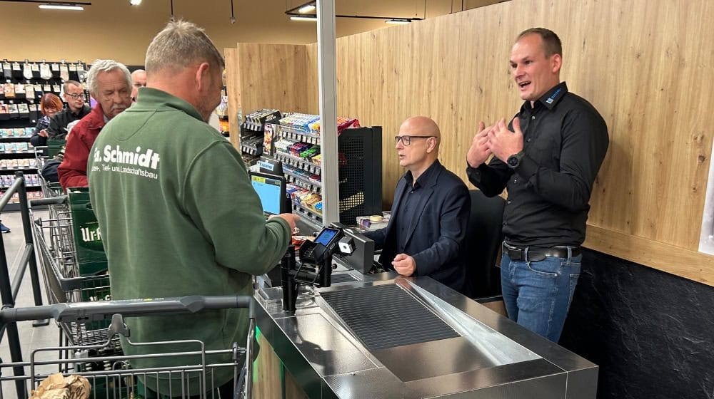 Bürgermeister Harry Habel unterstützt René Schäfer (r.) an der Kasse des neuen Supermarktes. Foto: meeco Communication Services GmbH