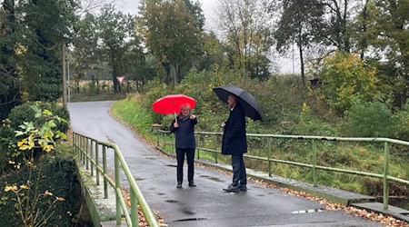 Stehen im Regen: Bürgermeisterin Michaela Ritter und Landrat Ralf Hänsel auf der Brücke über die Große Röder in Großdittmannsdorf Bildquelle: Landratsamt Meißen
