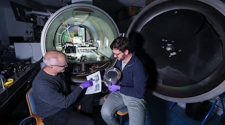 Daniel Spemann (links) und Lukas Pietzonka vom Leibniz-Institut für Oberflächenmodifizierung (IOM) bereiten einen Laborversuch mit einem Ionentriebwerk vor.  / Foto: Jan Woitas/dpa