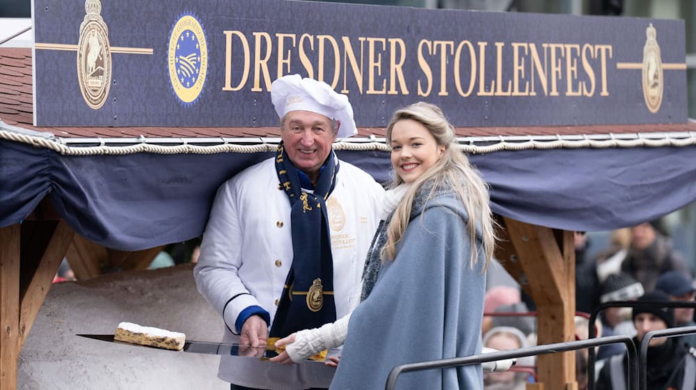 Master baker Reiner Israel and stollen girl Johanna Worm present a piece of the giant stollen at the Dresden Stollen Festival. / Photo: Sebastian Kahnert/dpa