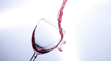 Rotwein schwappt aus einem schräg gehaltenen Weinglas und droht auszukippen.