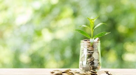 Münzstapel und Glas mit Münzen, aus denen kleine Pflanzen wachsen, als Symbol für nachhaltige Investitionen