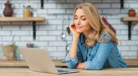 Frau sitzt in einer Küche am Laptop und informiert sich über sichere Online-Dienste und Datenschutz im Internet.