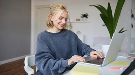 Junge Frau bearbeitet am Laptop in ihrer Wohnung ein Video oder Foto für ein kreatives Projekt