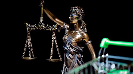 Statue der Justitia mit Waage vor schwarzem Hintergrund, im Vordergrund ein unscharfer Einkaufswagen mit grünem Griff als Symbol für Markt und Regulierung im Glücksspiel.