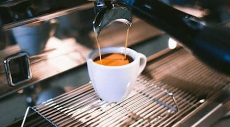 Frisch gebrühter Espresso fließt aus einer Siebträgermaschine in eine weiße Tasse auf dem Abtropfgitter.