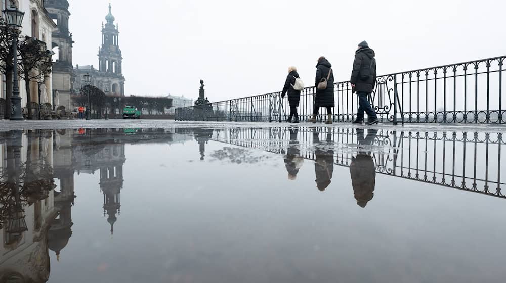 Passanten gehen auf der Brühlschen Terrasse vor der Katholischen Hofkirche in Dresden entlang. Ein regnerischer Start ins Wochenende erwartet die Menschen in Sachsen, Sachsen-Anhalt und Thüringen. / Foto: Sebastian Kahnert/dpa