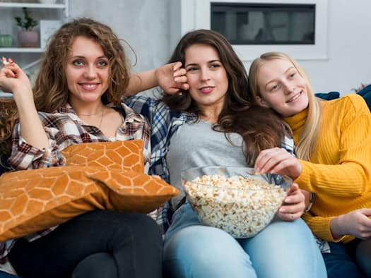 Drei Freundinnen schauen gemeinsam nostalgische Filme mit Popcorn