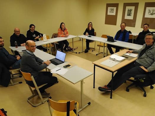 Eine Gruppe sitzt in einem Seminarraum vor Unterlagen und schaut lächelnd in die Kamera