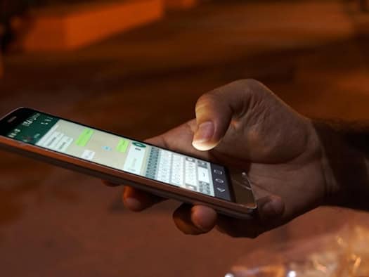 Person hält ein Smartphone in der Hand und nutzt eine Messaging-App, im Hintergrund unscharfe Abendbeleuchtung.