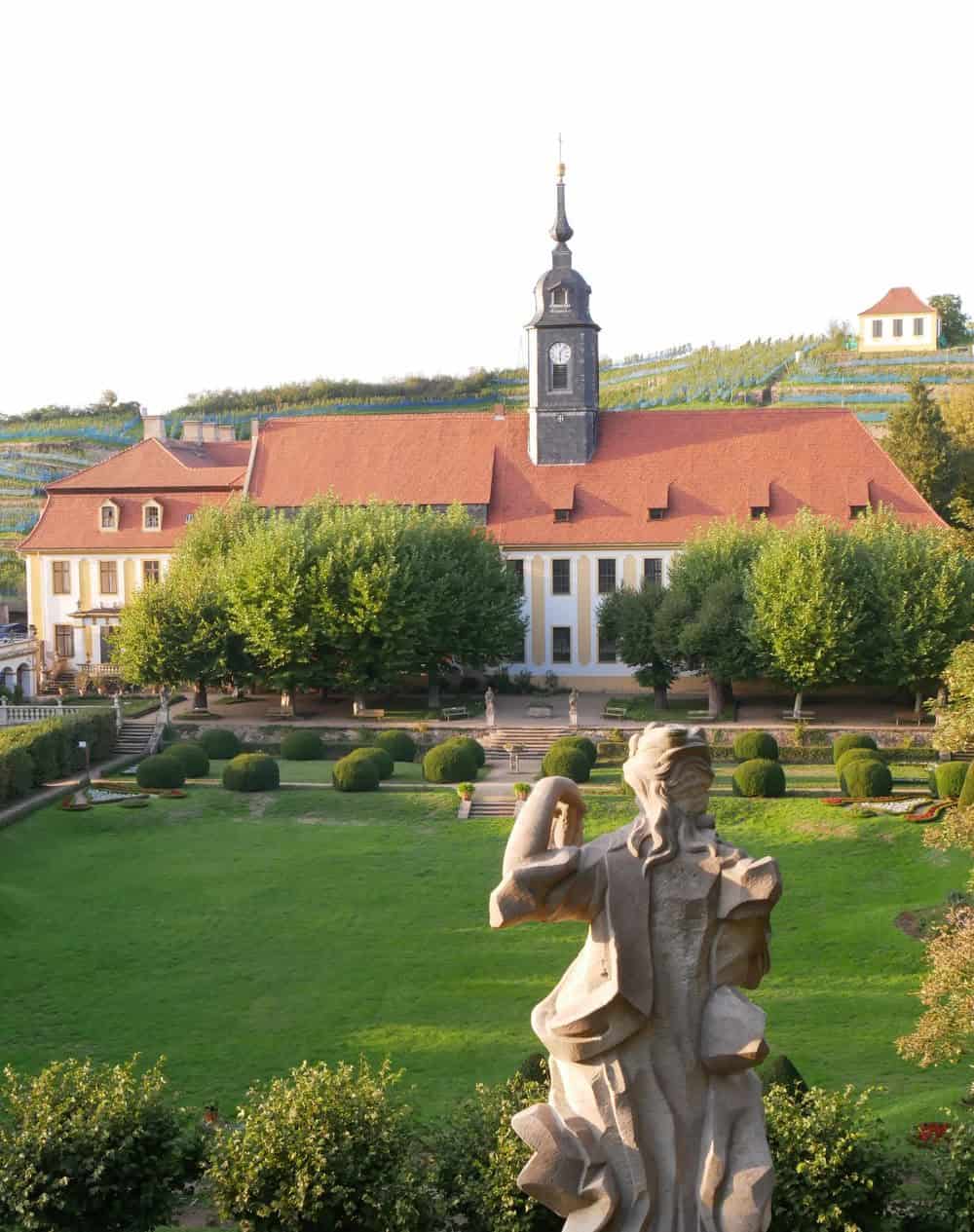 Foto: Blick über Park und Wiese auf eine Kirche, im Vordergrund eine Steinstatue