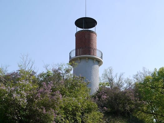Der Aussichtsturm Hoher Stein in Dresden-Plauen auf einem Felsplateau, umgeben von blühendem lila Flieder und grünen Bäumen unter strahlend blauem Himmel.