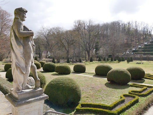 Foto: Blick auf eine gepflegte, winterliche Parkanlage mit Wiesen und Büschen, im Vordergrund eine Steinstatue, im Hintergrund ein bewaldeter Hügel