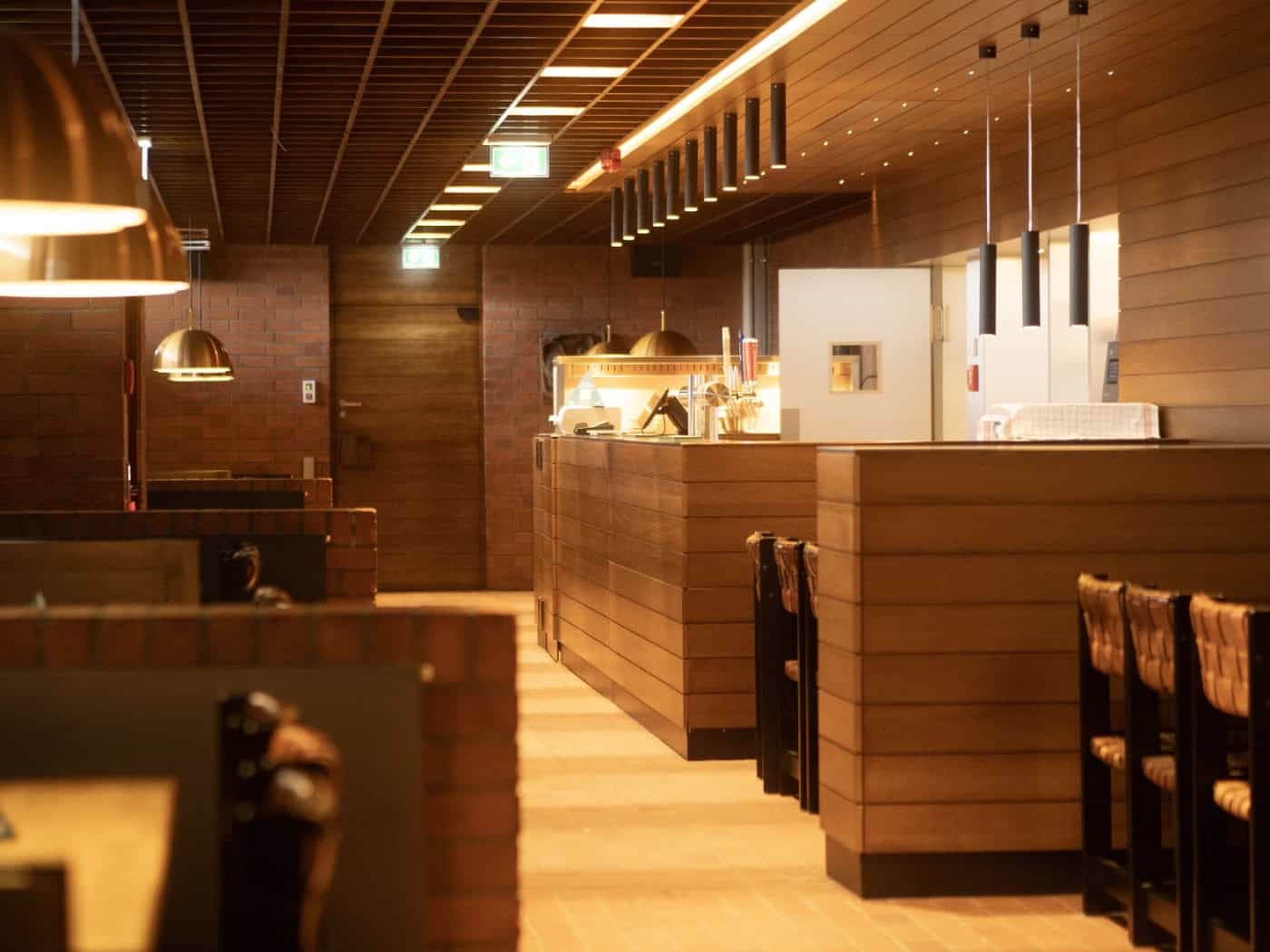 Innenansicht der sanierten Bierstube in der Neuen Mensa der TU Dresden mit markanten Ziegelwänden, Holzverkleidung und warmen Pendelleuchten.