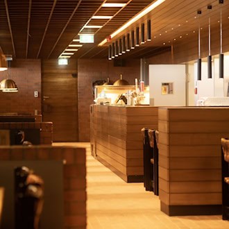 Innenansicht der sanierten Bierstube in der Neuen Mensa der TU Dresden mit markanten Ziegelwänden, Holzverkleidung und warmen Pendelleuchten.