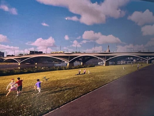Ein großer Flachbildschirm zeigt eine digitale Visualisierung (Rendering) der neuen Carolabrücke in Dresden. Im Vordergrund der Darstellung sieht man eine grüne Wiese mit spielenden Menschen an der Elbe, im Hintergrund die moderne Brückenkonstruktion.