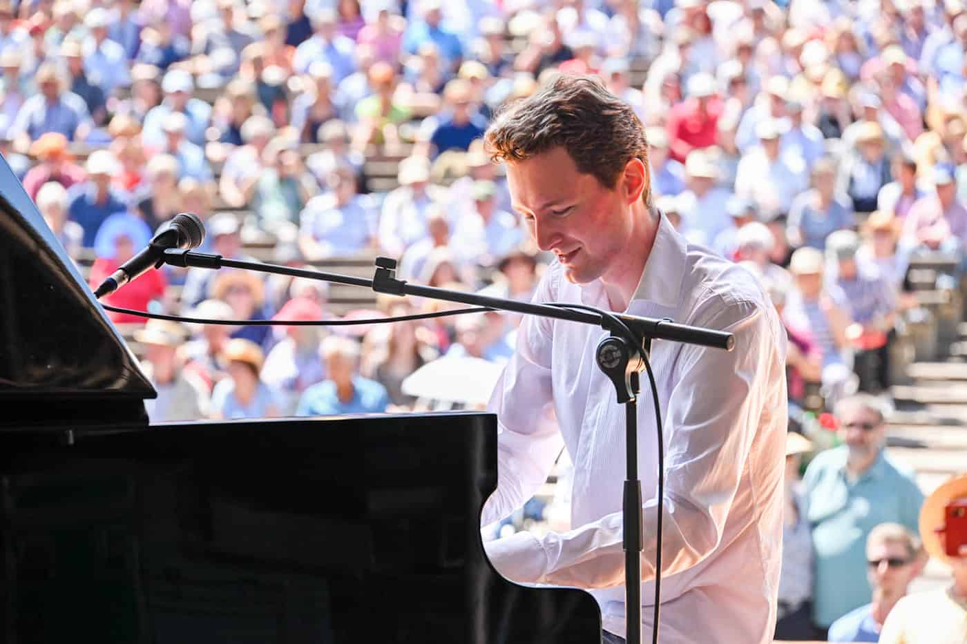 Pianist Dan Popek spielt konzentriert an einem schwarzen Flügel bei einem Open-Air-Konzert des Dixieland Festivals in Dresden; im Hintergrund ist ein großes, unscharfes Publikum in der Sonne zu erkennen.