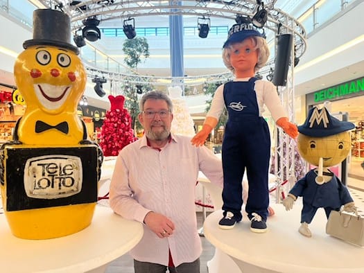 Sammler Torsten Meisel steht im Elbepark Dresden zwischen drei großen DDR-Werbefiguren: Das gelbe Telelotto-Männchen mit Aufschrift „Tele Lotto“, eine große Puppe in dunkelblauer Interflug-Uniform und das Leipziger Messemännchen mit MM-Logo auf dem Hut.