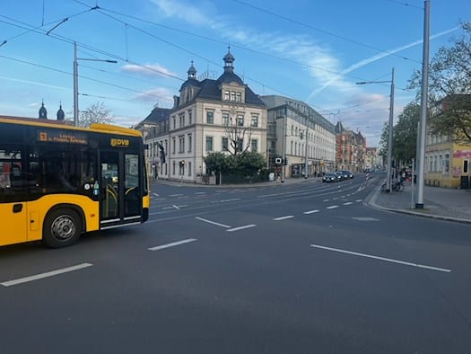 Ein gelber Bus der Dresdner Verkehrsbetriebe (DVB) passiert den Wasaplatz. Im Hintergrund sind historische Gebäude der Caspar-David-Friedrich-Straße und Oberleitungen der Straßenbahn zu sehen.