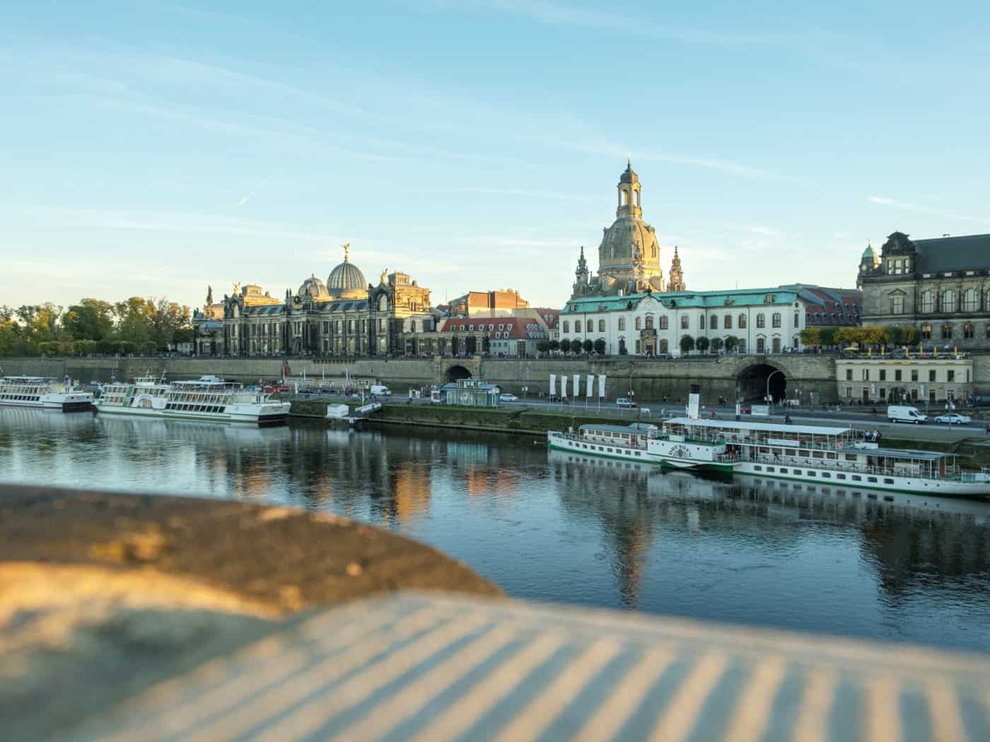 Blick über die Elbe in Dresden auf die historische Altstadt mit der Kunstakademie und der Frauenkirche. Im Vordergrund liegen mehrere Fahrgastschiffe der Weißen Flotte am Anleger. Das Bild symbolisiert das öffentliche Leben in Dresden.