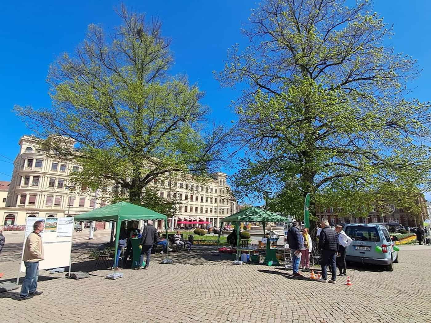 Foto: Infostände auf einem städtischen Platz bei Sonnenschein, ein paar Personen davor im Gespräch