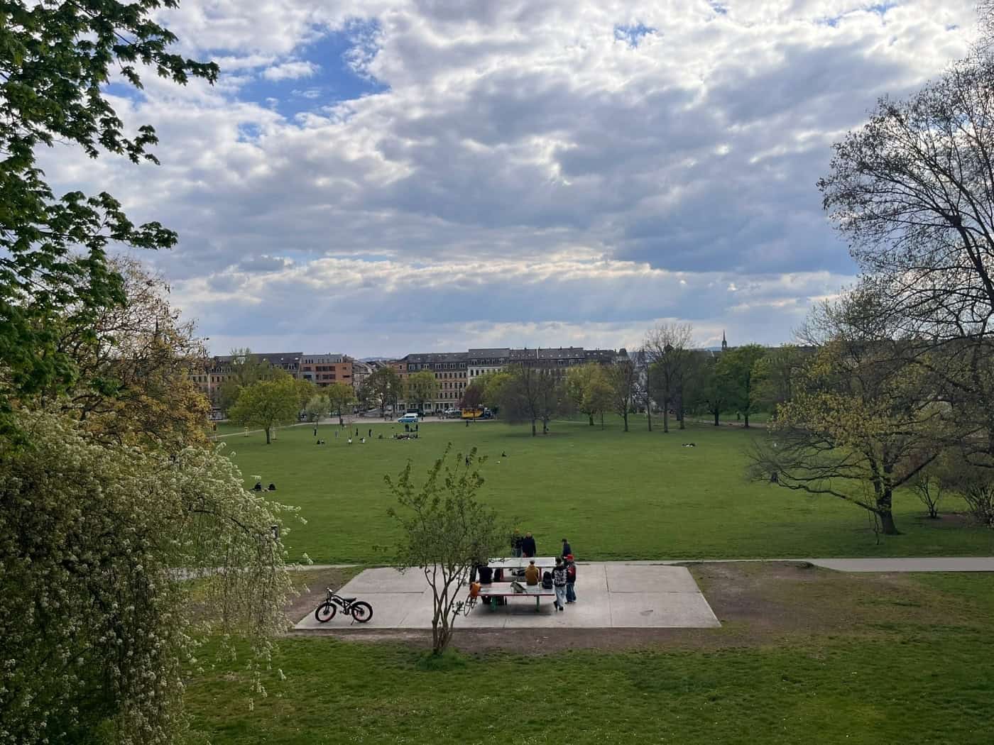 Weitwinkelaufnahme des Alaunparks von einer Anhöhe aus. Im Vordergrund spielen Menschen an einer Tischtennisplatte, dahinter erstreckt sich die große grüne Parkwiese bis zu den Gebäuden der Äußeren Neustadt.