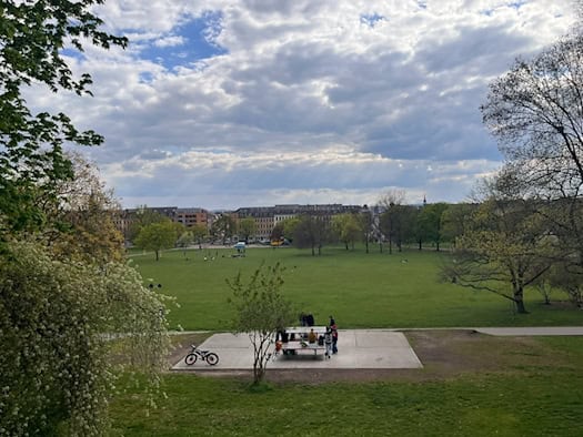 Weitwinkelaufnahme des Alaunparks von einer Anhöhe aus. Im Vordergrund spielen Menschen an einer Tischtennisplatte, dahinter erstreckt sich die große grüne Parkwiese bis zu den Gebäuden der Äußeren Neustadt.