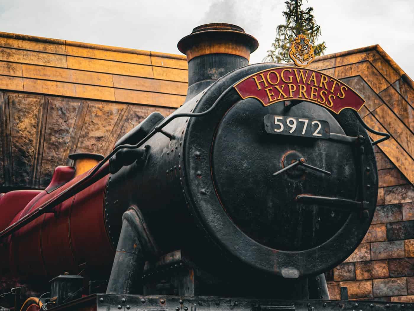 Nahaufnahme der schwarzen Dampflokomotive „Hogwarts Express“ mit der Nummer 5972. Dampf steigt von den Rädern auf, im Hintergrund ist eine rustikale Bahnhofsmauer aus Stein zu sehen. Das Bild steht symbolisch für die Harry Potter Wanderausstellung in Dresden.