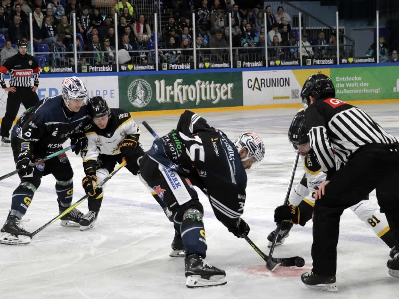Eishockeyspieler der KSW IceFighters Leipzig während eines Spiels auf dem Eis, umgeben von Schiedsrichtern und Zuschauern.