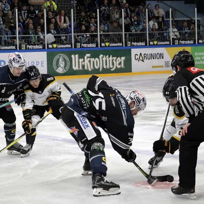 Eishockeyspieler der KSW IceFighters Leipzig während eines Spiels auf dem Eis, umgeben von Schiedsrichtern und Zuschauern.