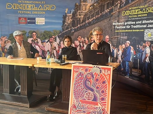 Pressekonferenz zum Internationalen Dixieland Festival Dresden 2026: Drei Organisatoren sitzen an einem Tisch vor einer großen Sponsorenwand; im Vordergrund lehnt ein buntes, illustriertes Plakat für die „Prohibitionsparty – Circus of Swing“.
