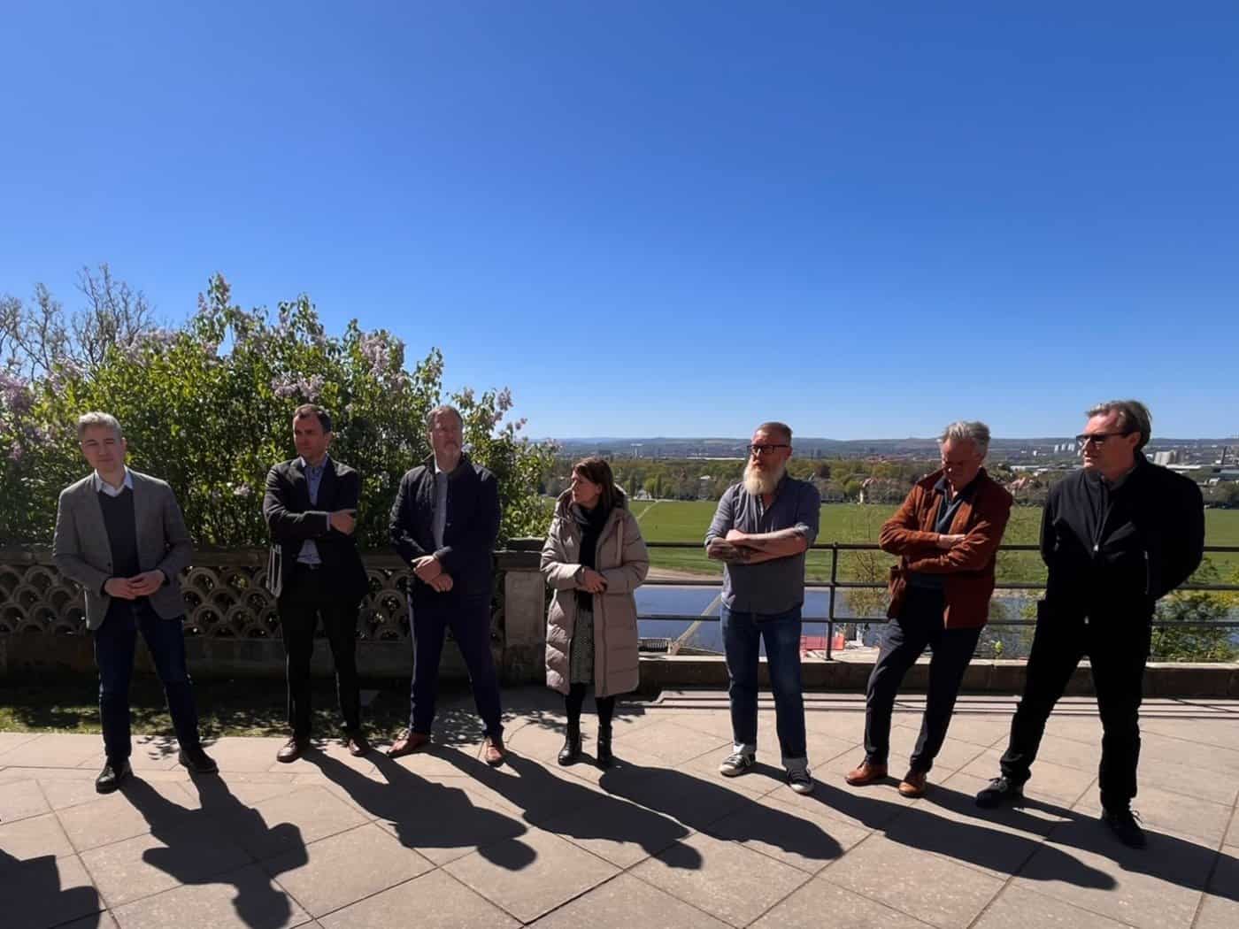 Sieben Personen stehen im Halbkreis auf der sonnigen Terrasse von Schloss Albrechtsberg vor dem Panorama des Dresdner Elbtals. Von links nach rechts: Stephan Kühn, Lars Knüpfer, Uwe Schmidt, Christiane Filius-Jehne, Lutz Müller, Carsten Dietmann und Mirco Meinel. Die Gruppe bildet den Vo