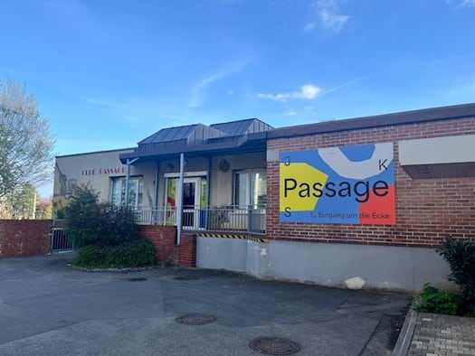 Außenansicht des Kulturzentrums Passage in Dresden-Gorbitz. Das flache Gebäude zeigt eine Kombination aus rotem Backstein und hellem Putz. Ein großes, modernes Schild der Jugendkunstschule (JKS) weist auf den Eingang hin, während an der Fassade noch der historische Schriftzug „Club Passage“ zu sehen