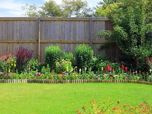 Blühender Garten mit Holzlattenzaun, farbenfrohen Staudenbeeten und gepflegtem Rasen als Beispiel für eine sichere und ästhetische Gartengestaltung.
