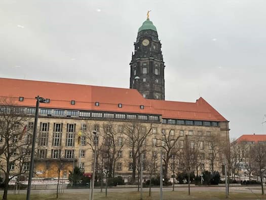 Das Neue Rathaus in Dresden mit seinem markanten, 68 Meter hohen Turm und dem Goldenen Rathausmann an der Spitze; im Vordergrund das Verwaltungsgebäude mit rotem Ziegeldach unter einem bewölkten Himmel.
