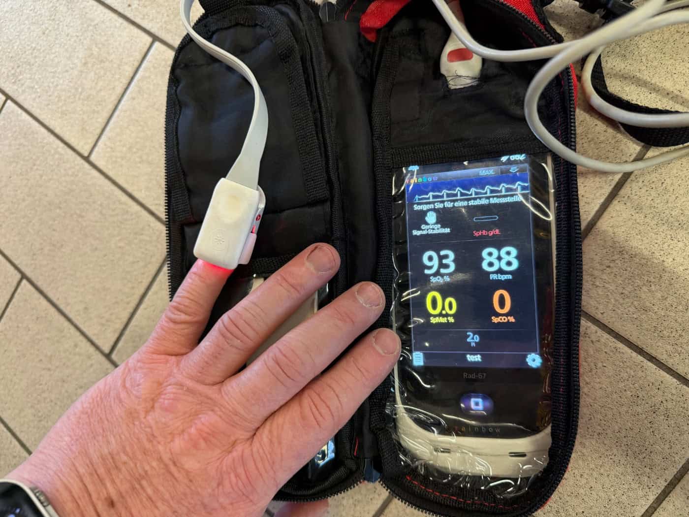 Ein medizinischer Sensor ist an der Fingerspitze einer Person befestigt und misst über Lichtsignale den Kohlenmonoxid-Gehalt im Blut. Das Display des kompakten Handgeräts zeigt den aktuellen Prozentwert an.