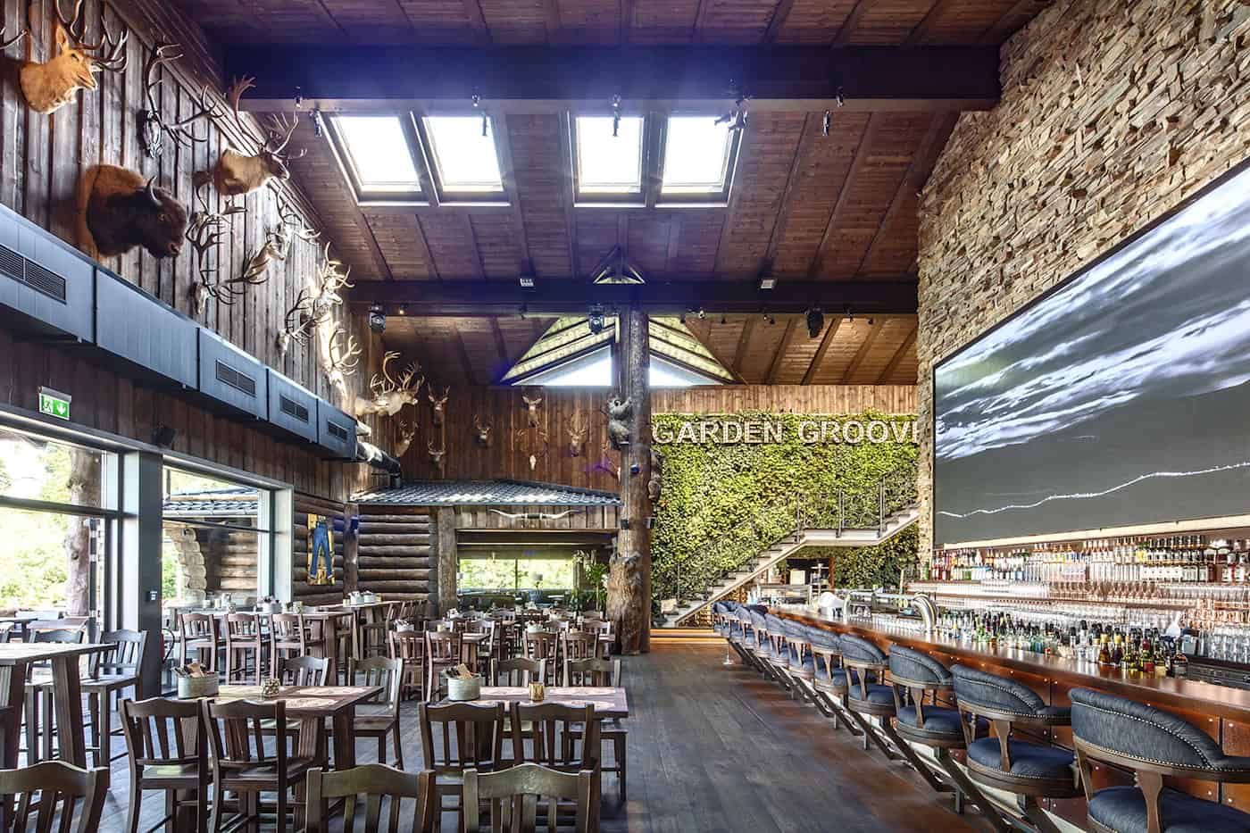 Innenansicht eines Timberjacks-Restaurants mit hohen Holzdecken, zahlreichen Hirschgeweihen an den Wänden, einer langen Bar mit beleuchtetem LED-Bildschirm und einem großen hölzernen Bären als Skulptur.