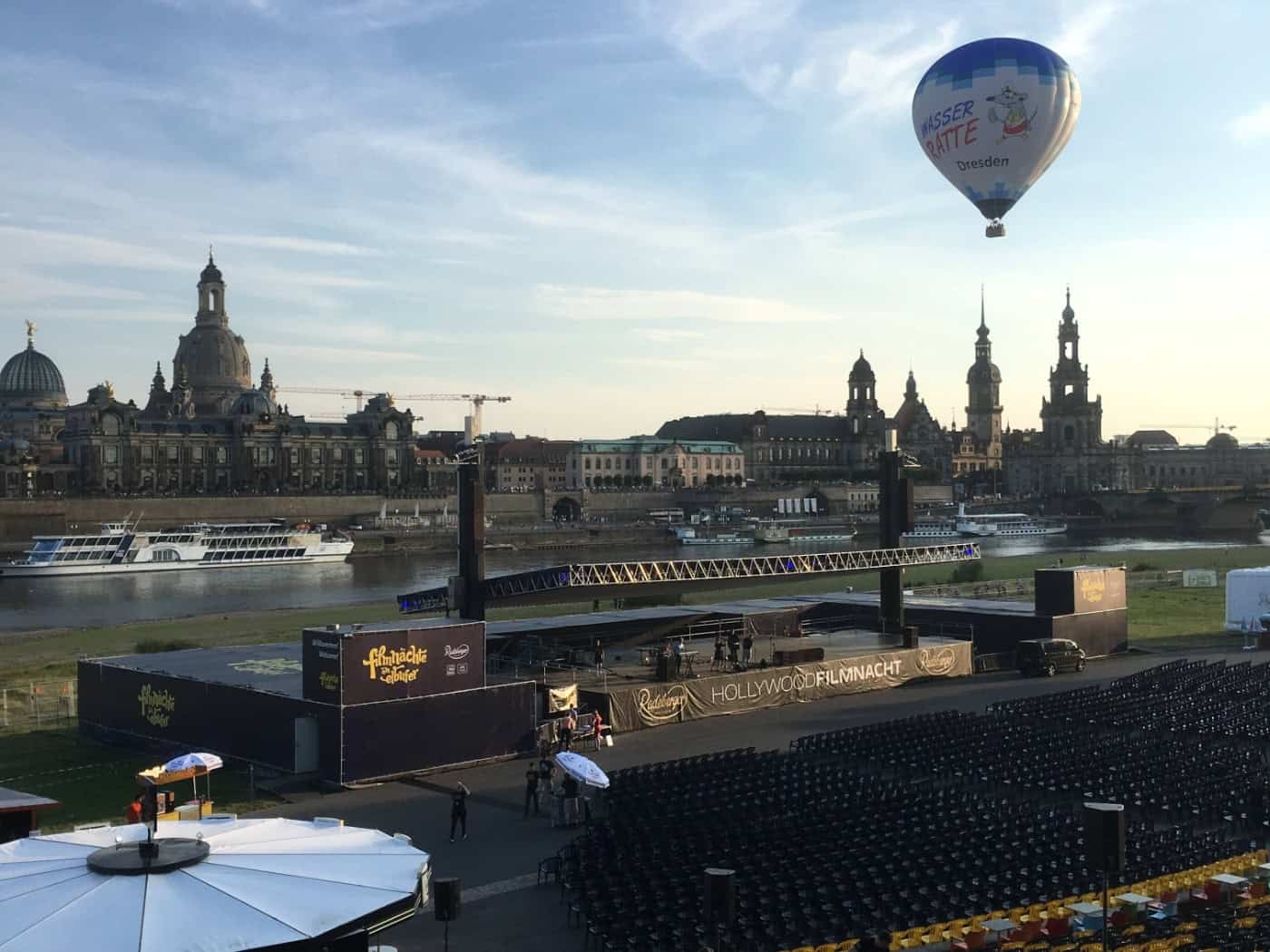 Blick über das Veranstaltungsgelände der Filmnächte am Elbufer in Dresden. Im Hintergrund die Elbe und die historische Altstadt bei klarem Himmel mit einem Heißluftballon.