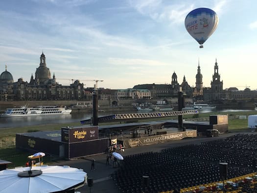 Blick über das Veranstaltungsgelände der Filmnächte am Elbufer in Dresden. Im Hintergrund die Elbe und die historische Altstadt bei klarem Himmel mit einem Heißluftballon.