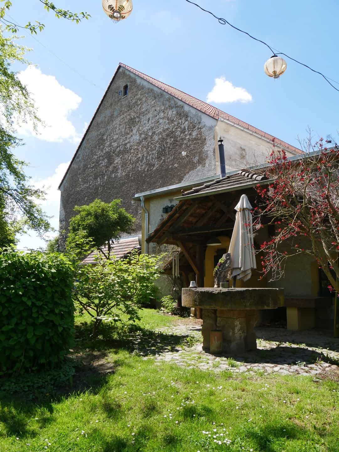 Foto: Hecken, Wiese und ein Steintisch im Vordergrund, im Hintergrund die Giebelseite eines Hauses