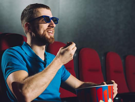 Mann mit 3D-Brille isst Popcorn im Kino – perfekt für Casino-Filme