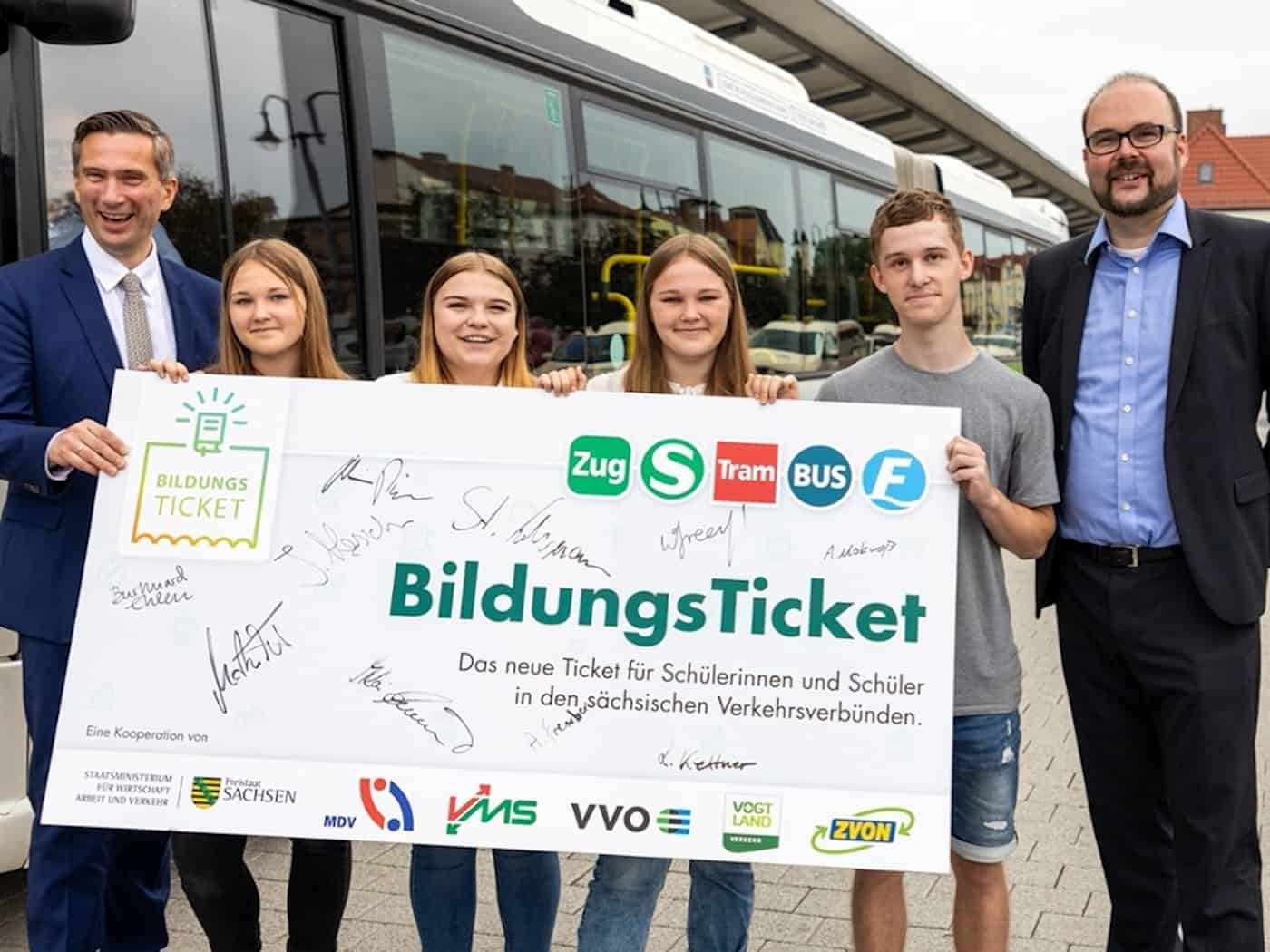 Archivbild von 2021: Martin Dulig und Christian Piwarz halten gemeinsam mit vier Jugendlichen ein großes Schild mit der Aufschrift „BildungsTicket“ vor einem weißen Linienbus. Das Schild trägt die Logos sächsischer Verkehrsverbünde und zahlreiche Unterschriften.
